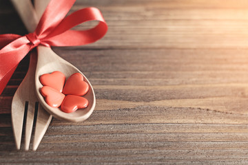 Wooden spoons and forks are strapped together with a bright red ribbon,red heart in wooden spoon placed on a wooden background,dinner for lover in valentines day.
