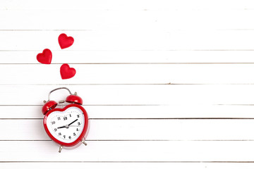 Heart-shaped alarm clock and hearts on white woooden background. Place for text. Top view.