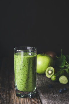 Green smoothie detox juice in glass on wooden table. Toned image, dark background