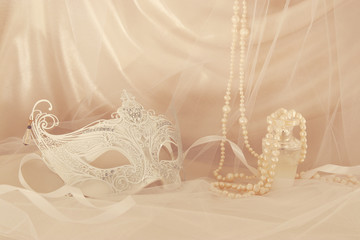 Image of delicate and elegant white venetian mask in front of tulle background.