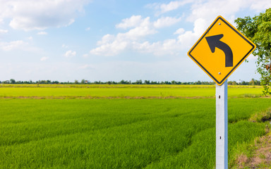 Yellow traffic sign on road with green nature rice field background .