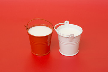 Red and white buckets with milk on a red background