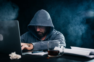 A hacker in a gray sweatshirt sits behind a laptop
