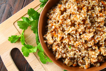 Boiled buckwheat in a bowl with pieces of chicken meat and cilantro on a brown wooden table.