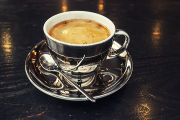 Cup of coffee on a black wooden table with a spoon reflection.