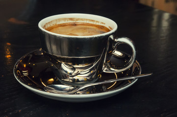 Cup of coffee on a black wooden table with a spoon reflection.