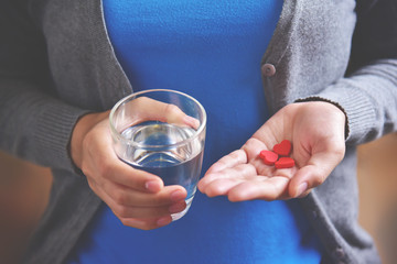 Female is holding red pills in heart shape.