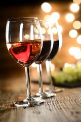 three glass of white red and rose wine with dim light in wooden restaurant table with a grape background