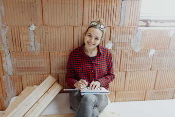 young, pretty, blonde woman with yellow helmet is planning on the notebook and tablet the expansion...