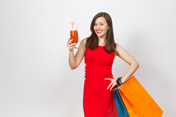 Attractive glamour fashionable young woman in red dress holding glass of drink cocktail, multi colored packets with purchases after shopping isolated on white background. Copy space for advertisement.