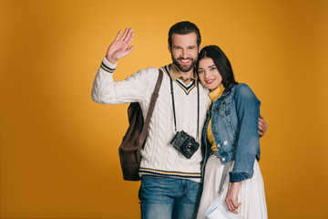 boyfriend waving hand and hugging girlfriend isolated on yellow