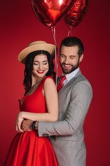 smiling stylish couple with red balloons isolated on red