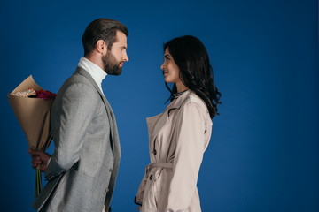 boyfriend hiding bouquet from girlfriend isolated on blue