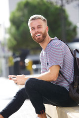 smiling male university student sitting outside with mobile phone