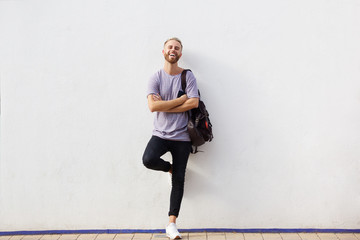 Full body happy young man with beard leaning against wall with arms crossed