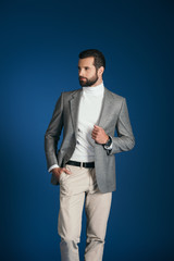 handsome man standing in suit and looking away isolated on blue