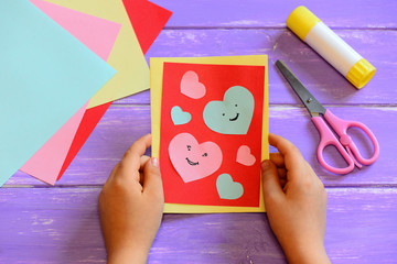 Child is holding a Valentines day card in his hands. Small child made a Valentines day greeting card. Cute and simple paper crafts for kindergarten. Closeup