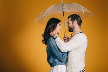 couple hugging under transparent umbrella isolated on yellow