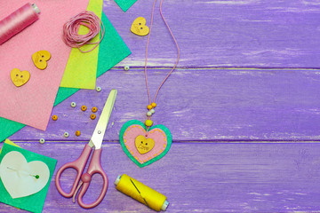Nice pendant necklace. Valentines day heart necklace made from felt, beads and wooden button. Handicraft supplies on a wooden background with copy space for text. Felt jewellery. Children crafts