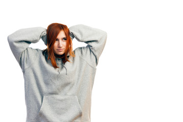 A young red-haired woman in a gray sweatshirt is holding herself with both hands behind her head, which is ill on a white isolated background