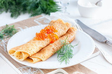 Homemade pancakes with red caviar and fresh herbs on a white plate, horizontal