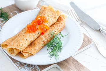 Homemade pancakes with red caviar and fresh herbs on a white plate, horizontal