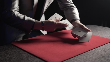 A magician makes a magic trick and reveals 4 aces over a red carpet during a show in a casino