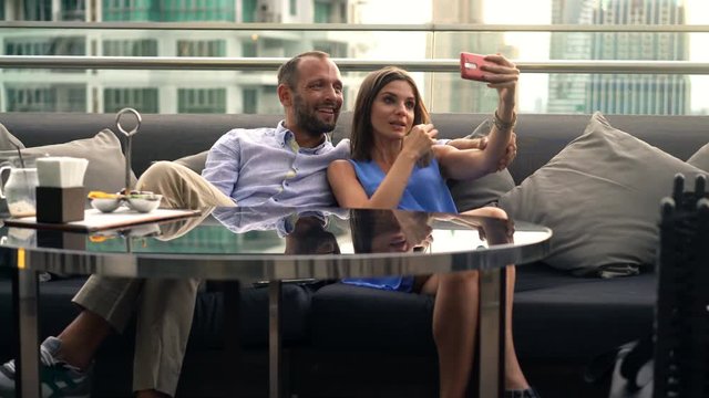Young, happy couple taking selfie photo with cellphone in bar on terrace
