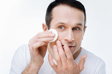 Clean skin. Nice handsome pleasant man holding a cotton pad and cleaning his skin while caring about it