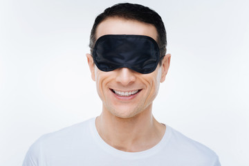 Ready to sleep. Delighted positive nice man smiling and wearing a sleeping mask while being ready to sleep