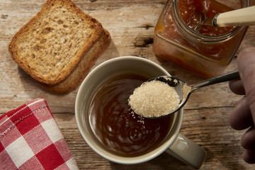 versando zucchero in una tazza con the caldo con fette biscottate e marmellata per la colazione 