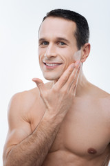 Perfect face. Nice happy delighted man smiling and enjoying the smoothness of his skin while standing against the white background