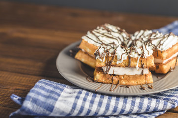waffles with cream and chocolate on plate on wooden table.