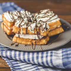 waffles with cream and chocolate on plate on wooden table.