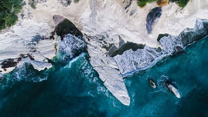 Aerial view of landmark big white chalk rock at Governor's beach caves, Limassol, Cyprus. The steep stone cliffs and deep blue sea waves crushing in coves and dark sand from above.