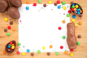 Obraz premium Easter concept painted and chocolate eggs, sweets, drops, candys for holiday with place for text pattern on wooden light background with paper
