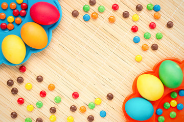 Easter concept painted and chocolate eggs, sweets, drops, candys for holiday with place for text pattern on wooden light background