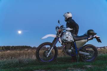Naklejka na ściany i meble Active way of life, enduro motorcycle, a guy looks at the stars at night and the moon, unity with nature, the spirit of adventure, escape from the hustle and bustle of the city, travel concept