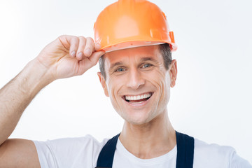 Ready to work. Cheerful happy nice man fixing his helmet and smiling while being ready to work