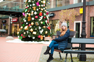 Pretty red haired woman wearing winter outfit, posing on the background of Christmas spruce