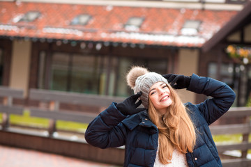 Fototapeta premium Happy red haired woman wearing black winter coat and knitted hat posing at the street in Kiev