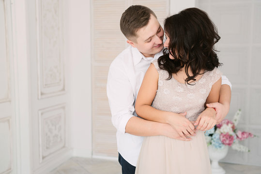 Young cheerful european couple in love embracing and kissing in decorated studio, light pastel colors, dating.