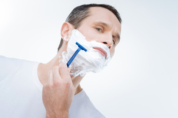 True man. Handsome nice pleasant man holing a razor and using it while shaving his face