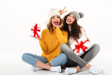 Two happy girls in sweaters and hats sitting with gifts