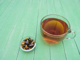 A glass cup of black tea on a mint-colored wooden table