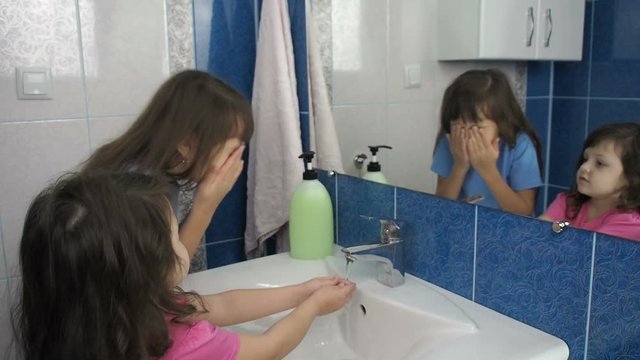 The children washes. Little girls wash their faces in the bathroom in front of the mirror.