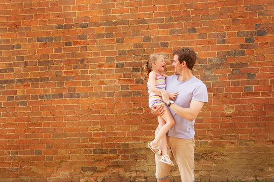 Girl laughing in father's arms by brick wall