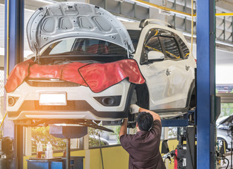 Fototapeta premium Car on lift to repair suspension in the garage with mechanic working underneath lifted car to change wheel hub and maintenance repair at service station 