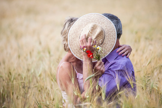 Couple in field in tall grass covering faces with straw hat