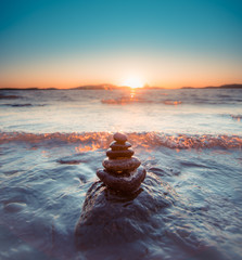 Round smooth stones in pyramid form by sea with wave coming in during golden sunset
